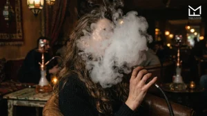 Woman smoking hookah in a lounge while enjoying the Love66 shisha flavour.